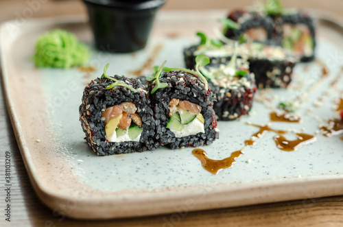 Set of rolls of black rice, fish and philadelphia cream cheese, sesame seeds, on a white plate, poured with unagi sauce and microgreen sprouts, side view