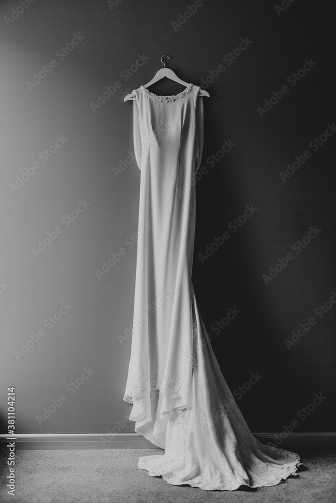White wedding dress of the bride with a train on a hanger on a nail on a gray wall.