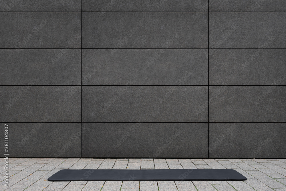 empty and blank foldable black yoga mat on grey sidewalk near empty street  outdoor in front