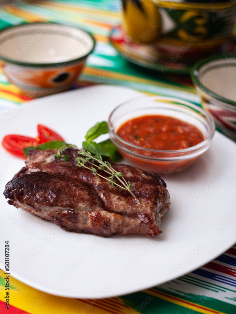 beef steak with tomato sauce, tomatoes and herbs in oriental style on a table with a teapot and a cup for tea. beef steak with tomato sauce, tomatoes and herbs in oriental style on a table with a teapot and a cup for tea.