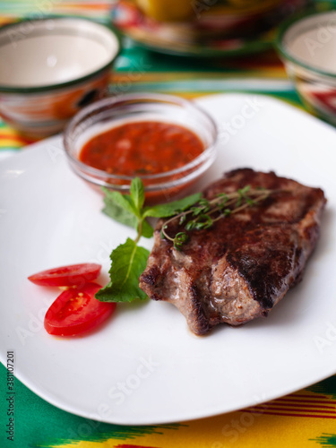 beef steak with tomato sauce, tomatoes and herbs in oriental style on a table with a teapot and a cup for tea.