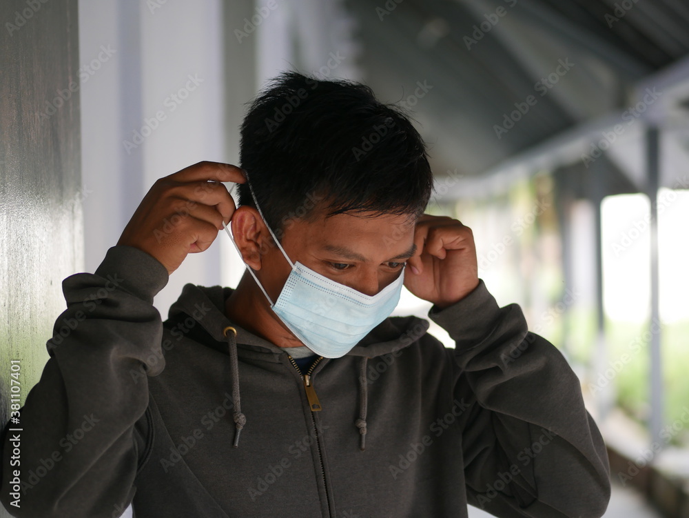 Closeup shot of an Indonesian young man using a medical mask during the Covid-19 pandemic. Handsome Indonesian guy wears a surgical mask to protect himself from coronavirus