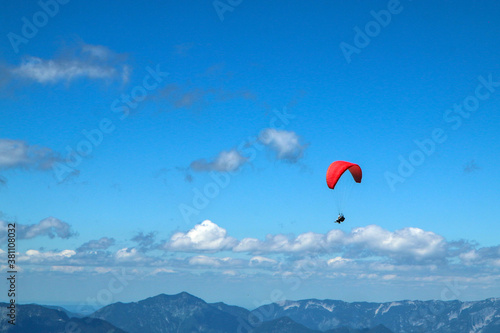 The paraglides are flying above the mountains high in the blue sky and enjoying the view. 