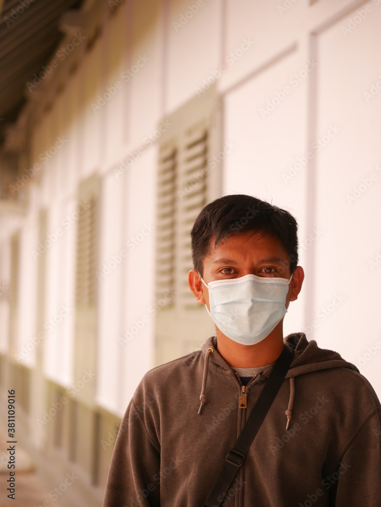 Protrait of an Indonesian young man using a medical mask during the Covid-19 pandemic. Handsome Indonesian guy wears a surgical mask to protect himself from coronavirus
