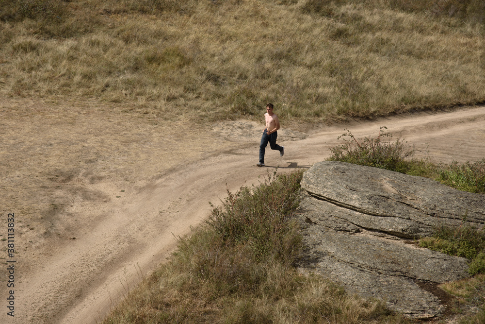 A young man runs on a dirt road. View from above.