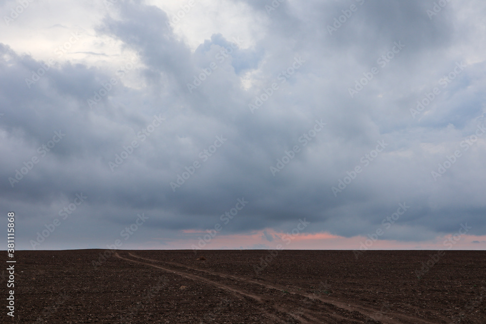 Autumn cultivated land rural bare field with dirt road going to horizon with dramatic sunrise colored gorgeous clouds. Plowed field with grey epic sunset layered cloudscape Autumn cultivated land rural bare field with dirt road going to horizon with dramatic sunrise colored gorgeous clouds. Plowed field with grey epic sunset layered cloudscape