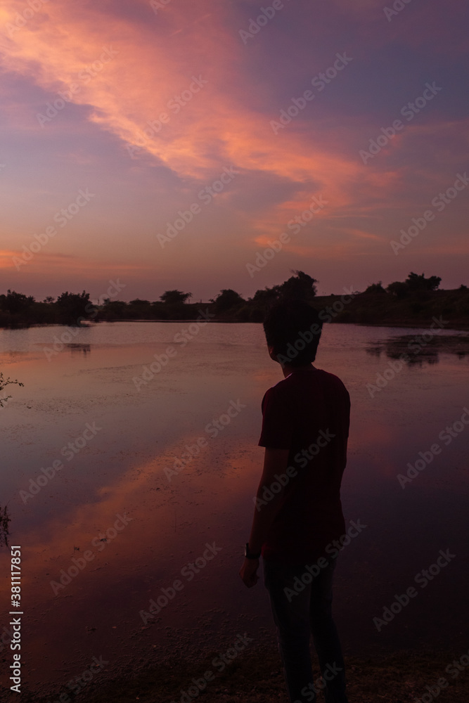 Fototapeta premium Silhouette of an Indian man standing in front of the lake during the sunset