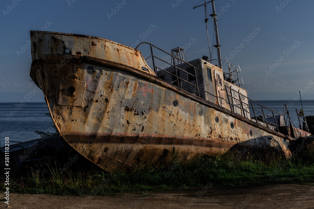 old rusty fishing boat, ship on grassy shore of lake Baikal, sea in light of setting sun