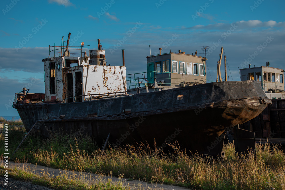 old rusty ships, boats, vessels on grassy shore in light of sunset, coast of lake Baikal, blue sky