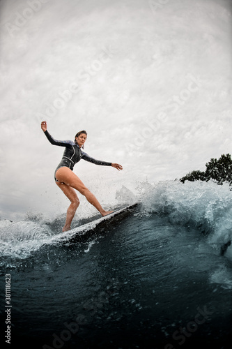 young woman confidently stands on the wake surf board and rides the wave.