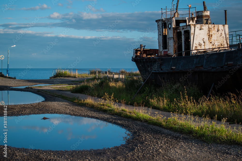 Fototapeta premium old rusty white ship, boat on grassy shore in light of sun, near round puddles on coast of lake Baikal, blue sky