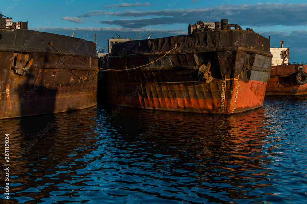 Old rusty red brown barges at sea, reflected in blue water in sunset light. Lake Baikal. Beautiful seascape with abandoned boats