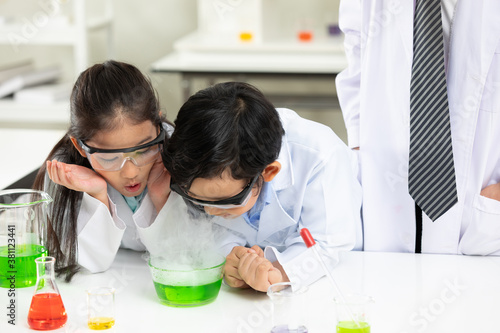 child student doing or testing a chemical experiment with science teacher by them side in laboratory classroom