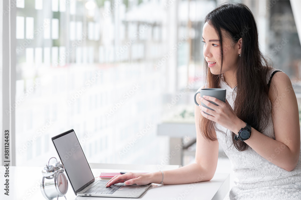 Portrait of young attractive woman holding cup of coffee and using laptop with happiness while sitting in modern co-workspace room. Portrait of young attractive woman holding cup of coffee and using laptop with happiness while sitting in modern co-workspace room.