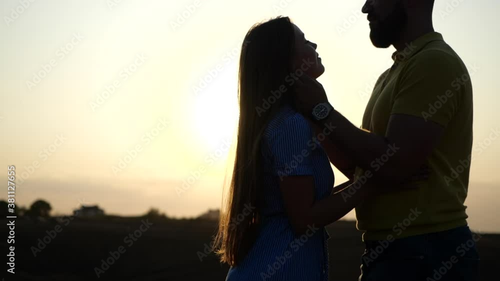 Romantic date of kissing loving happy young european couple outdoors in field against backdrop of summer sunset in slow motion. Close-up view of bearded guy with clock hug beautiful girlfriend in sun. Romantic date of kissing loving happy young european couple outdoors in field against backdrop of summer sunset in slow motion. Close-up view of bearded guy with clock hug beautiful girlfriend in sun.