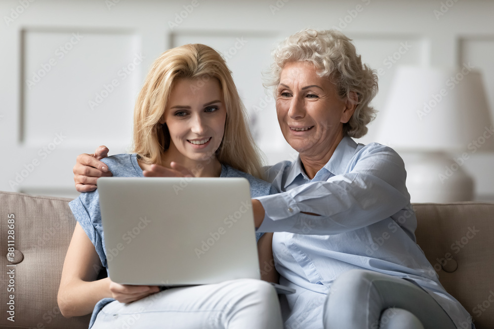 Look, mommy, it is easy. Caring grown up daughter teaching explaining retired mother how to work with laptop apps, happy old grandmother sits on couch with adult grandchild watching video on pc screen Look, mommy, it is easy. Caring grown up daughter teaching explaining retired mother how to work with laptop apps, happy old grandmother sits on couch with adult grandchild watching video on pc screen