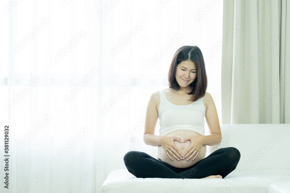 Asian pregnant woman holding her hands in a heart shape on her belly