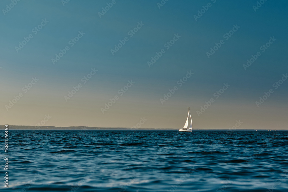 Sailing boat or yacht with open white sails floating on the sea at sunset. Majestic landscape, calm and tranquility