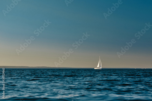 Sailing boat or yacht with open white sails floating on the sea at sunset. Majestic landscape, calm and tranquility © Kostiantyn