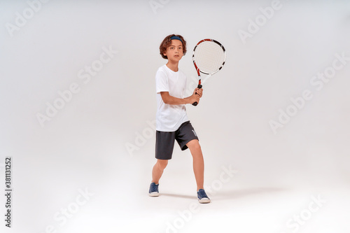 Active lifestyle. Full-length shot of a teenage boy holding tennis racket and looking away isolated over grey background © Kostiantyn