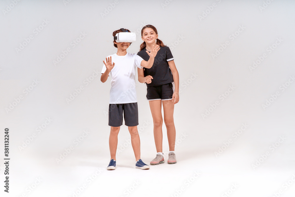 Virtual reality and sport. Two excited teenage, boy wearing 3d glasses and cute girl standing isolated over grey background and having fun Virtual reality and sport. Two excited teenage, boy wearing 3d glasses and cute girl standing isolated over grey background and having fun