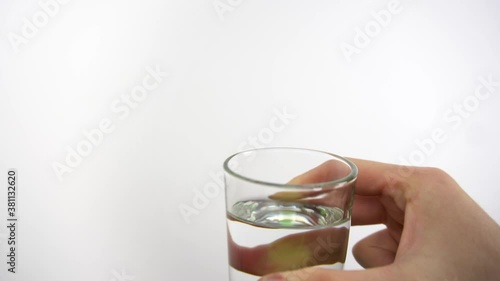 Man's hand is holding clear glass with water and drinks from it. Closeup of male hand in studio with white background acting drinking in first person view. Theme of taking different liquids inside. photo