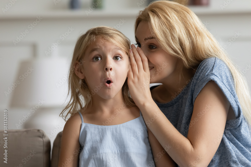 It is a great unknown. Smiling adult mom telling cute story as big mystery on ear of surprised little daughter, creative young nanny finding way to heart of small preschool child sharing funny secret It is a great unknown. Smiling adult mom telling cute story as big mystery on ear of surprised little daughter, creative young nanny finding way to heart of small preschool child sharing funny secret