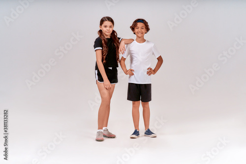 Getting ready to exercise. Two teenagers, cute boy and girl in sportswear looking at camera and smiling while posing isolated over grey background