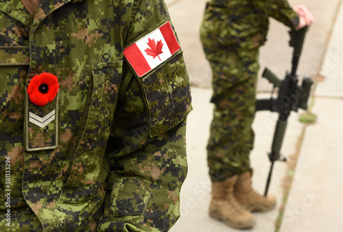 Obraz na plátně Flag of Canada on the military uniform and soldier with weapon on the background