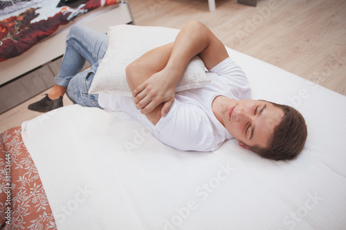 Top view shot of a young man hugging a cushion, lying in a be, relaxing at home