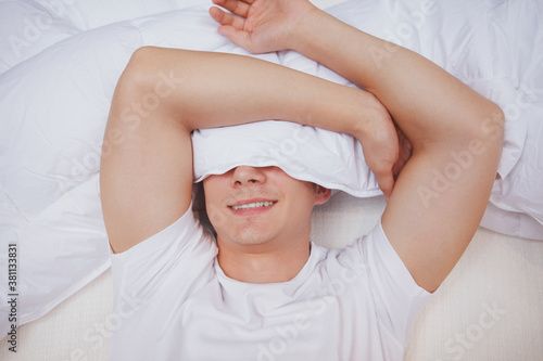 Top view close up of a happy young man lying in his bed covering half of his face with a blanket