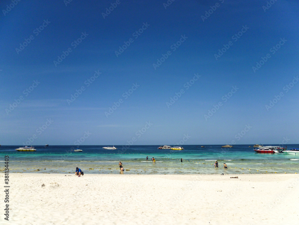 The shore of the Andaman Sea in Thailand with swimming tourists and boats waiting for them.
