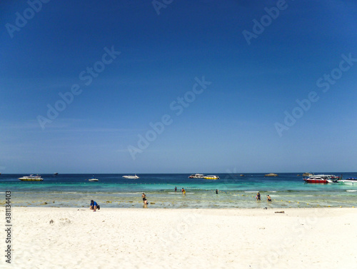 The shore of the Andaman Sea in Thailand with swimming tourists and boats waiting for them.