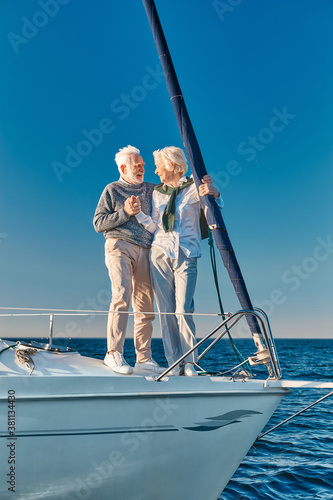 Vacation. Full length of happy senior couple in love holding hands and looking at each other while standing on the side of sailboat or yacht deck floating in sea © Kostiantyn