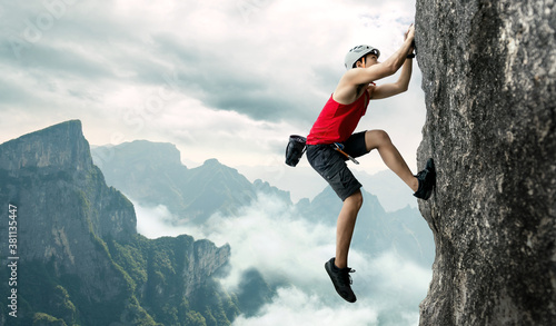 Foto Asian man rock climber in black pants climbing on the cliff.