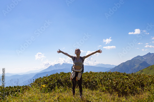 A girl stands on top of a mountain hands up, freedom, happiness concept