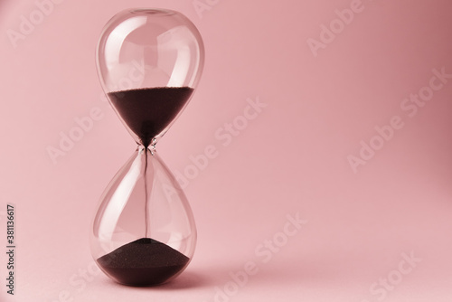 Hourglass on pink background, closeup. Urgency and running out of time concept