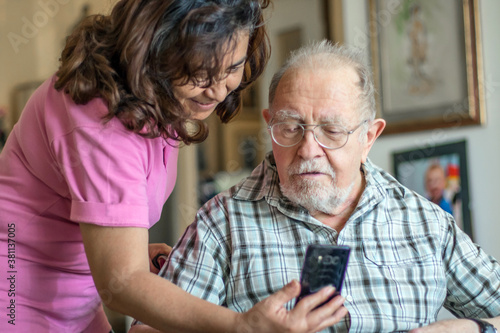 Smiling senior man and caregiver with smartphone are doing a videocall © Lsantilli