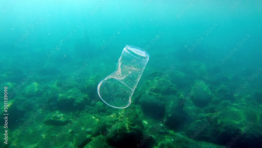 Underwater footage of a discarded plastic cup floating and bobbing suspended and submerged and