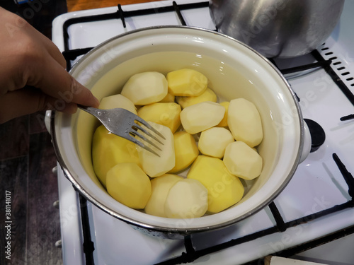 Raw potatoes are cooked in water. Cooking potatoes in a pot. Test readiness with a metal fork. photo