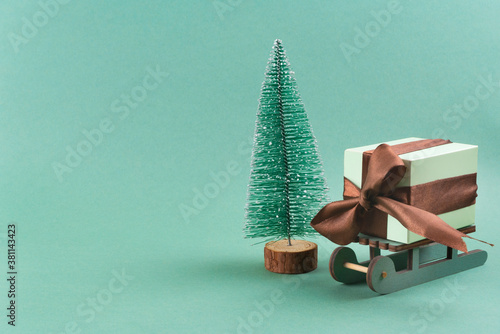 The gift lies on the sleigh next to the Christmas tree on turquoise background . christmas concept. postcard.