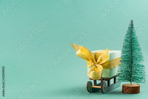 The gift lies on the sleigh next to the Christmas tree on turquoise background . christmas concept. postcard.