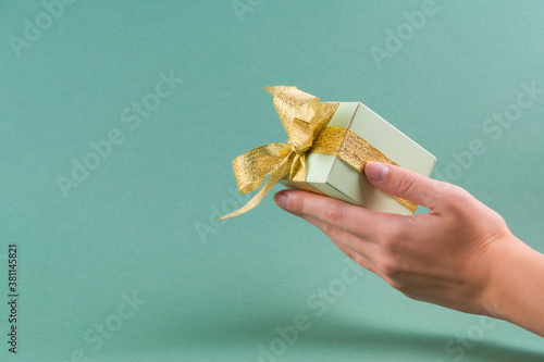 Female hands holding green gift box decorated with golden ribbon on turquoise background.christmas concept. copy spase
