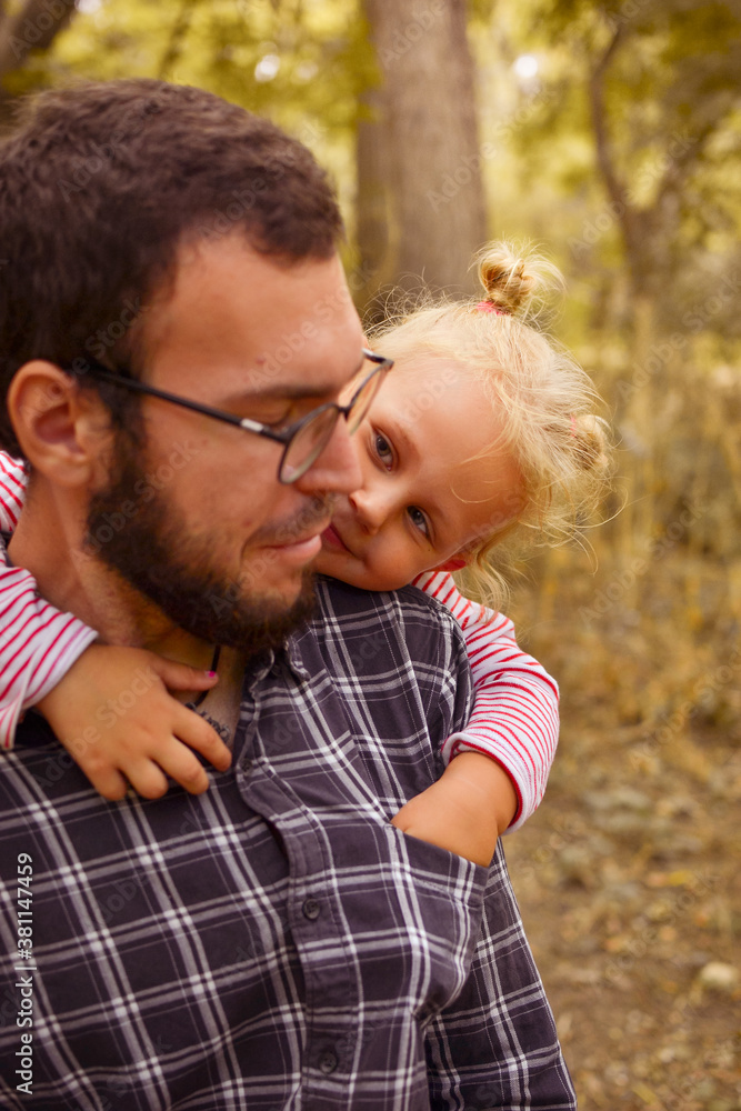 Fototapeta premium The baby hugs dad. Father holds a cute little girl in his arms. Autumn portrait of a child. Happy family and childhood moments.