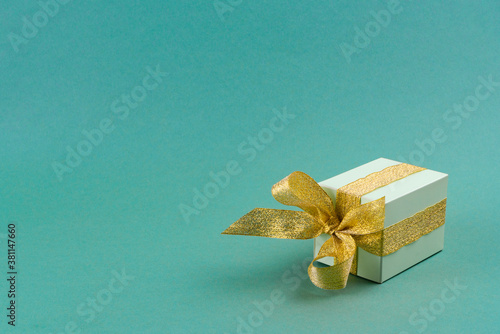 green gift box decorated with golden ribbon on turquoise background.christmas concept. copy spase