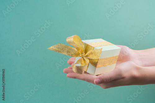 Female hands holding green gift box decorated with golden ribbon on turquoise background.christmas concept. copy spase