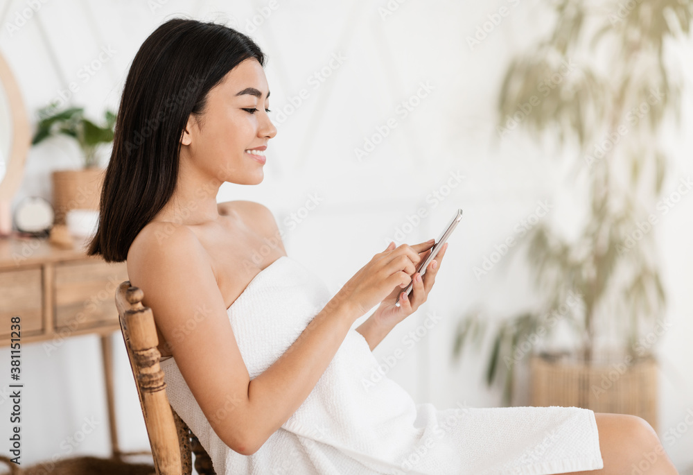 Asian woman in towel using smartphone, reading beauty blog Asian woman in towel using smartphone, reading beauty blog