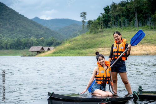 Two Asian girls in orange life jackets One person holds a paddle, the other sits, against the backdrop of water and mountains Ready for travel as a hobby in mae ngat dam, chiangmai