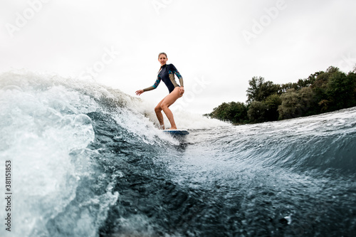Smiling woman in wetsuit rides down on surf style wakeboard on wave