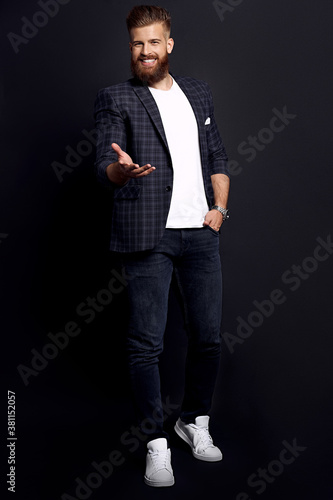 Confident and handsome. Full length of young man with ginger beard in smart-casual clothes smiling looking at camera while posing against black background
